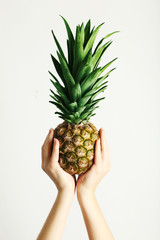 Female hands holding ripe pineapple on a white background