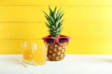 Ripe pineapple with glasses of juice on a white wooden table