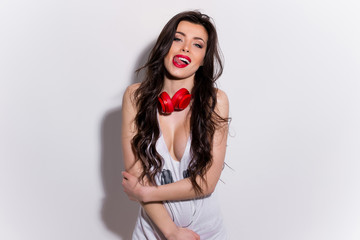 Young, happy and sexy girl with red lips with headphones in a t-shirt showing tongue and licking teeth - obrazy, fototapety, plakaty