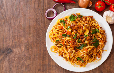 spaghetti with mushroom, vegetables and minced meat in a plate on wooden table