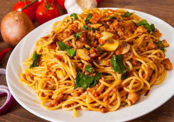 spaghetti with mushroom, vegetables and minced meat in a plate on wooden table