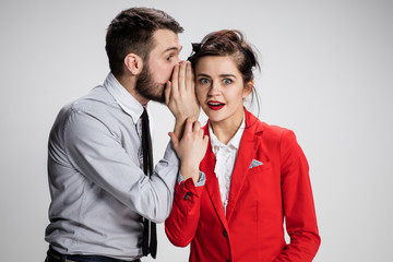 Young man telling gossips to his woman colleague at the office