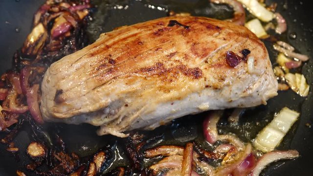 Frying a large piece of  meat with onions in a frying pan