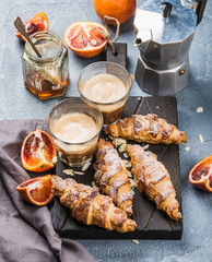Traditional Italian style home breakfast. Latte in glasses, almond croissants and red bloody Sicilian oranges over concrete textured table
