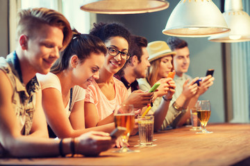 happy friends with smartphones and drinks at bar