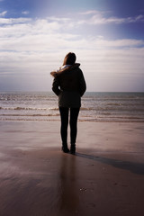 Back of a young woman standing on the beach looking out to sea