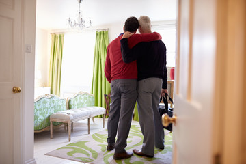 Male couple with arms around each other arrive in hotel room