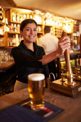 A young woman working behind a bar looking to camera