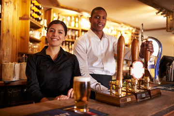 A young man and woman working behind a bar look to camera