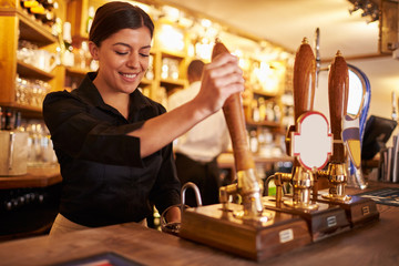 A young woman working behind a bar preparing drinks