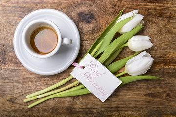 cup of coffee, white tulips and card with good morning written on wooden table top view