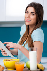 Young woman using a tablet computer, working or catching up on her social media, while having breakfast at home