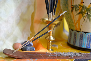 Burning incense sticks. 
Oriental elements as burning incense sticks, oriental ceramic vase and semiprecious stones are at silk fabric.