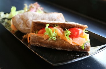 Sandwich with smoked salmon on black plate.