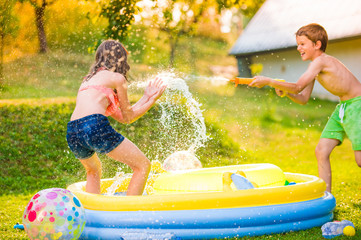 Boy splashing girl with water gun, garden swimming pool