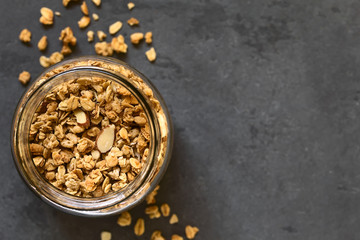 Crunchy almond and oatmeal granola in jar, photographed overhead on slate with natural light (Selective Focus, Focus on the top of the granola)
