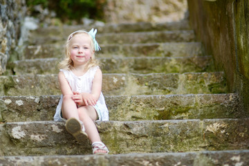Adorable little girl sitting on stairs on warm and sunny summer day © MNStudio