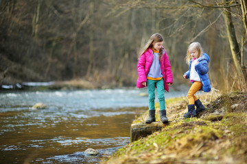 Two cute little sisters playing with a stick by a river