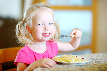 Obraz na płótnie Canvas Cute funny little girl eating spaghetti