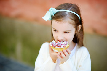 Adorable little girl eating fresh sweet strawberry cake outdoors on warm and sunny summer day