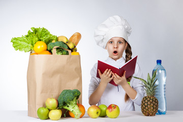 Little girl in a cap cook a variety of fresh food. Girl holds red book in hands. Wonder human...