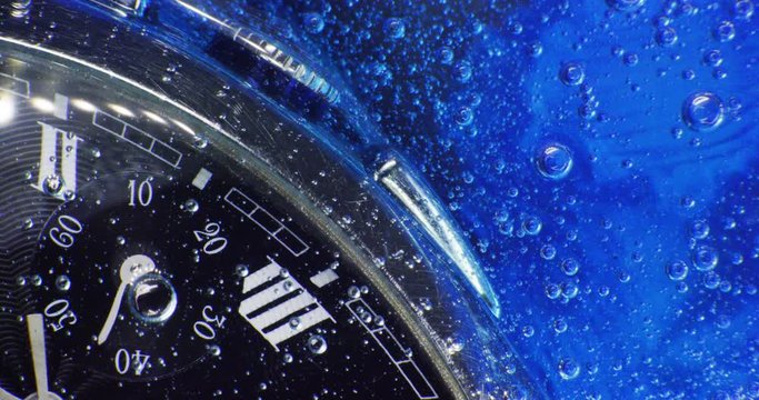 luxury man watch in the blue gel with moving bubbles and arrows. Extreme Macro close-up shot.
