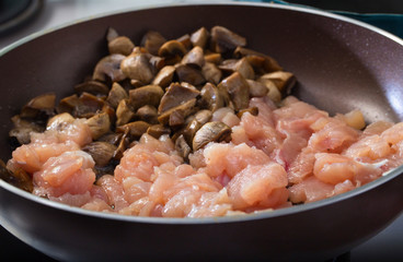 Crude chicken meat and mushrooms on a frying pan