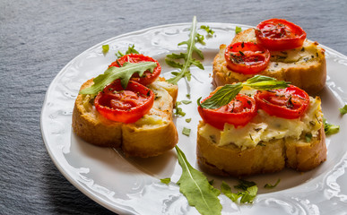 Toasts (Crostini) with ricotta, cherry tomatoes and arugula on black background. 