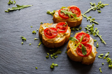 Toasts (Crostini) with ricotta, cherry tomatoes and arugula on black background. 