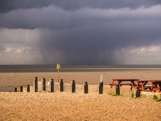 Whitstable, Kent, UK, beach. Rain cloud with rain falling on the horizon out at sea over old sea...