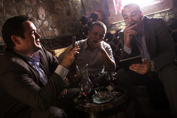 Three businessmen sitting in the wine cellar drinking wine and smoke cigar, resting after a hard day at work.