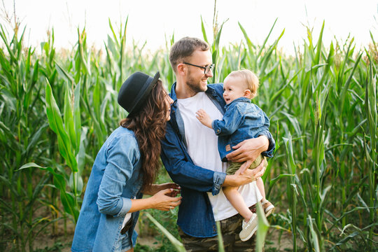 Young hipster father mother holding cute baby in corn field