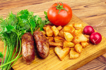 Grilled meat sausages with fried potatoes, tomato and fresh produce on wooden board