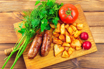 Grilled meat sausages with fried potatoes, tomato and fresh produce on wooden board, top view