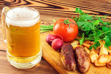 Grilled meat sausages with fried potatoes, fresh produce and mug of beer on wooden board
