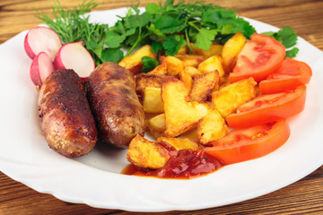 Grilled meat sausages with fried potatoes, sliced tomatoes, fresh produce and ketchup in plate on wooden table