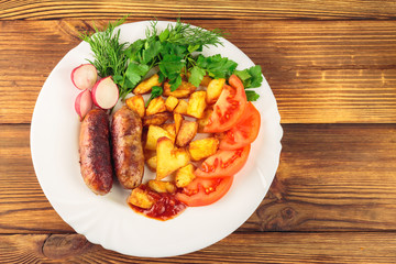 Grilled meat sausages with fried potatoes, sliced tomatoes, fresh produce and ketchup in plate on wooden table