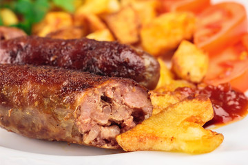 Cut grilled meat sausages with fried potatoes, sliced tomatoes and ketchup in plate, selective focus