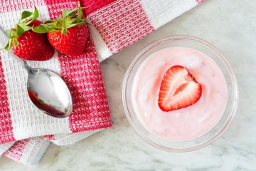 Strawberry flavored yogurt with fresh berries and checked cloth, overhead view on white marble - Powered by Adobe