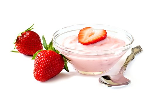 Clear bowl of strawberry flavored yogurt with spoon and fresh berries over a white background
