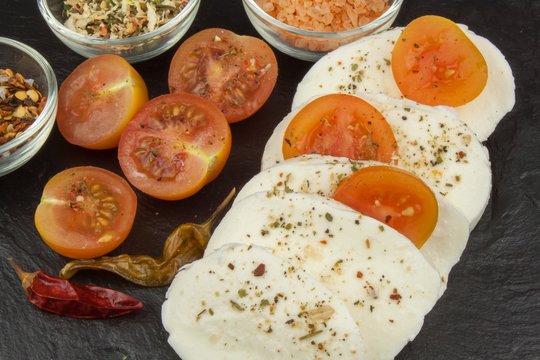 Fresh mozzarella cheese on slate board. Healthy diet meals. Preparing food for guests. Traditional meal. Mozzarella and tomatoes. Dark grey background.
