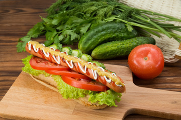 Spicy hotdog with fresh vegetables lying on wooden kitchen board