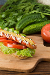 Spicy hotdog with fresh vegetables lying on wooden kitchen board