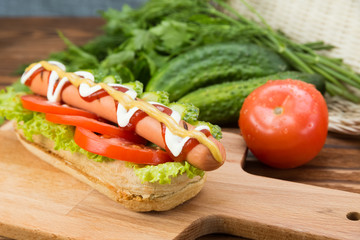 Spicy hotdog with fresh vegetables lying on wooden kitchen board