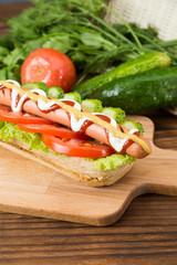 Spicy hotdog with fresh vegetables lying on wooden kitchen board