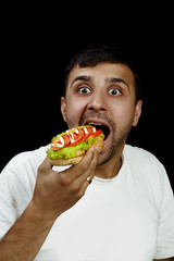 Young armenian man eating a messy hotdog isolated on black background