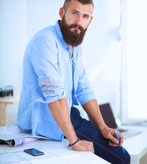 Portrait of male designer in hat with blueprints at desk 