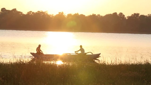 Fishermen rowing wooden canoe at sunset on Bendiwewa lake in Polonnaruwa, Sri Lanka