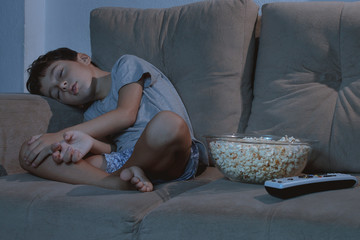 Small boy sleeping on the couch while watching TV and eating pop