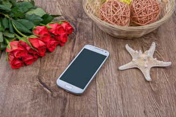 Mobile phone, white starfish and roses on a wooden background